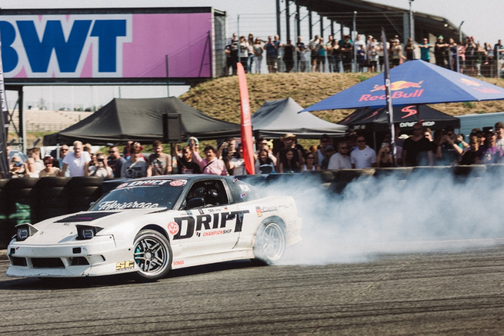 Nissan S13 drift car on track producing tire smoke during a drift event with ST suspensions branding.